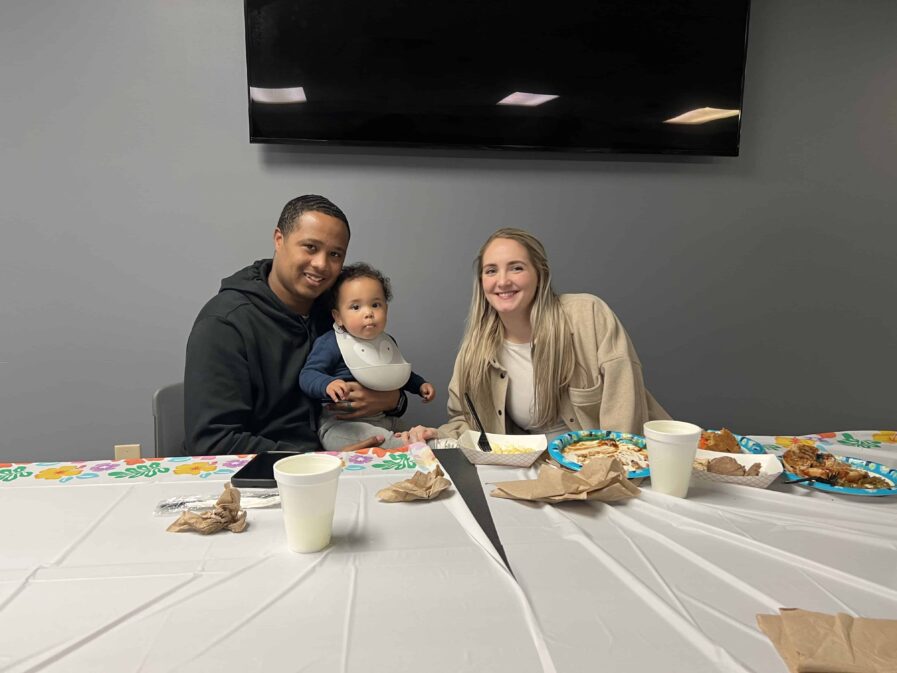 two students pose with baby at a dinner table