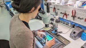 Woman looking through a microscope at electronic components