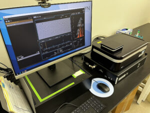 Instrument and computer on a laboratory bench with sample data on the screen.