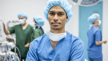 Asian doctor wearing scrubs and surgical cap in operating theatre, front view