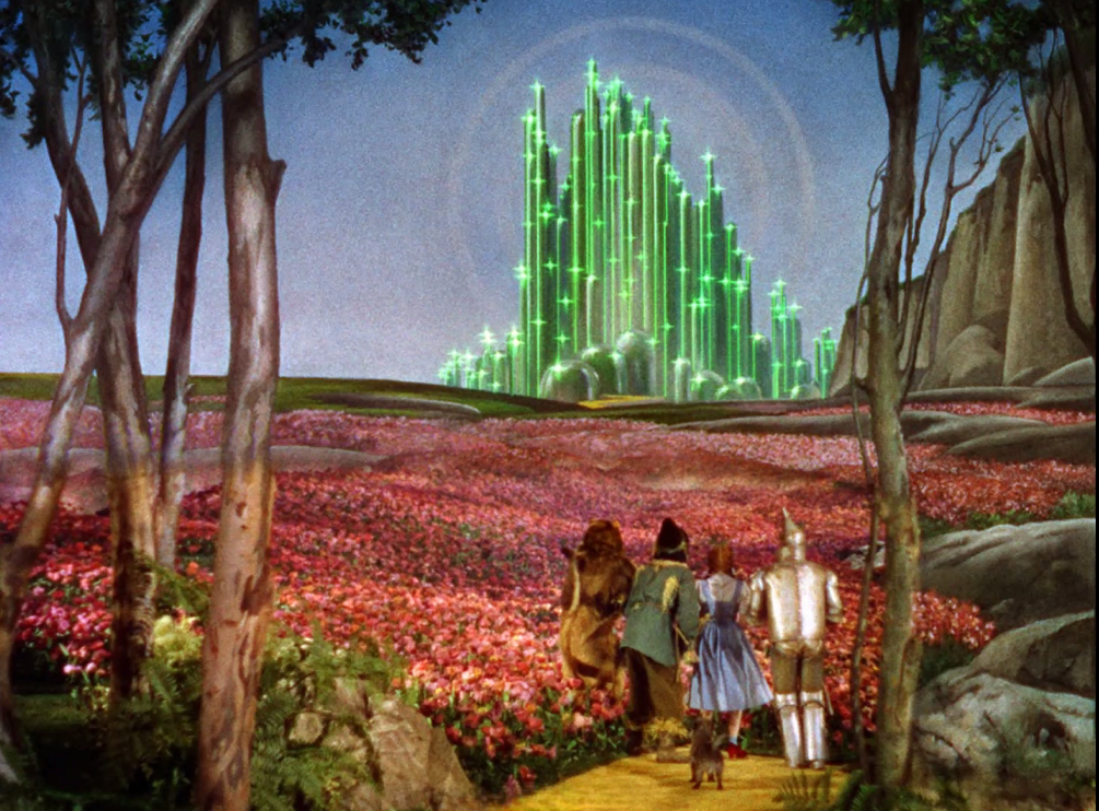 Dorothy, lion, scarecrow and tin man looking at emerald city with field of poppies before them.