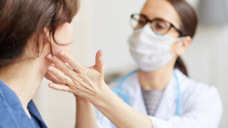 Young woman sitting while the nurse examining her throat during visit at hospital
