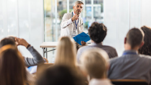 Male doctor talking to large group of people on a seminar in a board room.