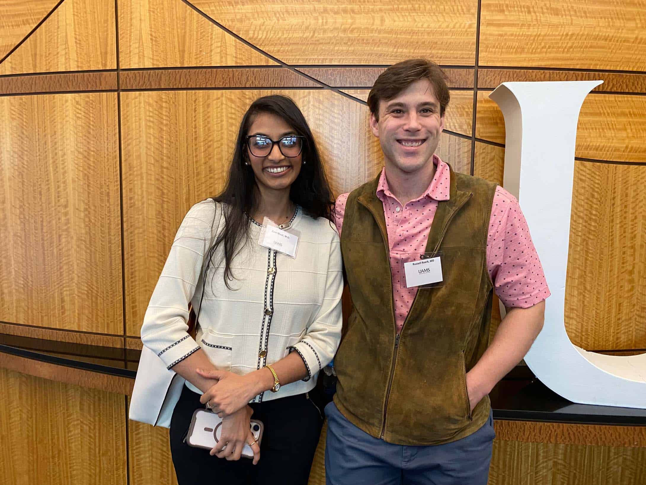 Two people standing in front of a wall with the UAMS sign