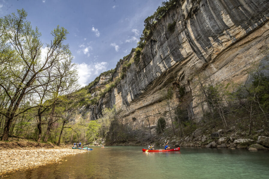 people in a canoe on the Buffalo River, next to large cliffs
