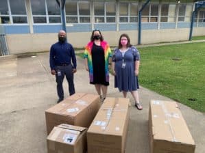 Three people posing outside a school with boxes of scientific equipment