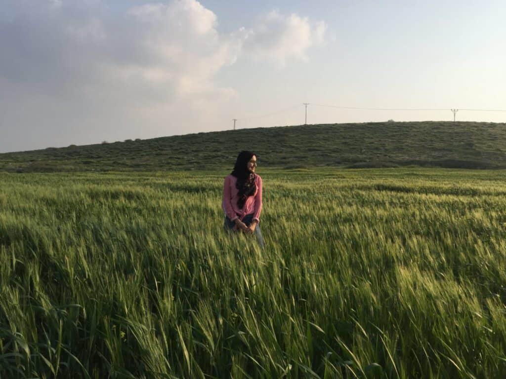 Bayan Alqtishat, M.D., sitting in a green field. The horizon and clouds are in the background.