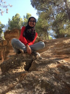 Dr. Alqtishat sitting on a large rock outside in a wooded area