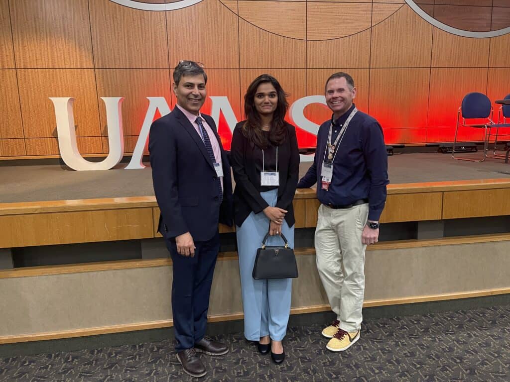 three people posing outside the conference in front of large letters that read UAMS.
