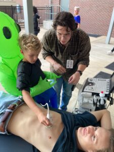 child and volunteer using a portable sonograph machine on a volunteer's chest