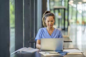 A woman wearing scrubs diligently studies at a desk in a modern educational building.