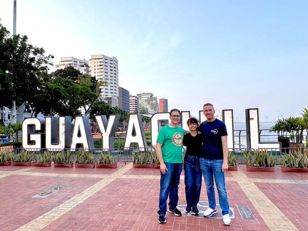 Larry Hartzell, Mary Timbang and Jeff Dorrity standing in front of a sign that reads Guayaquil