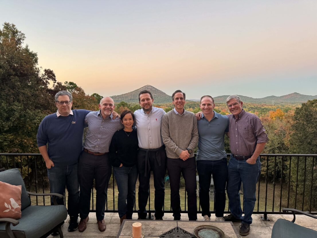 Faculty standing on a balcony with autumn trees and a mountain in the background