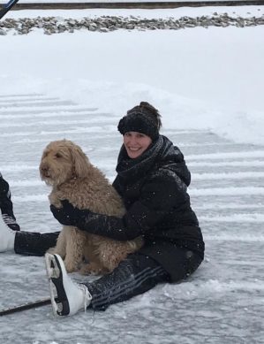 Woman sitting on a frozen lake with a dog. She is wearing ice skates.