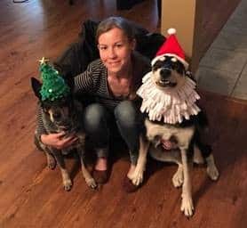 Woman posing with two dogs, who are wearing Christmas hats.