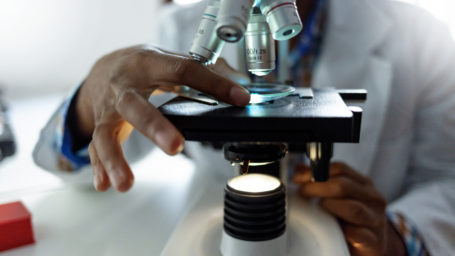 Photo of African-American scientist looking in microscope while working on medical research in modern laboratory.