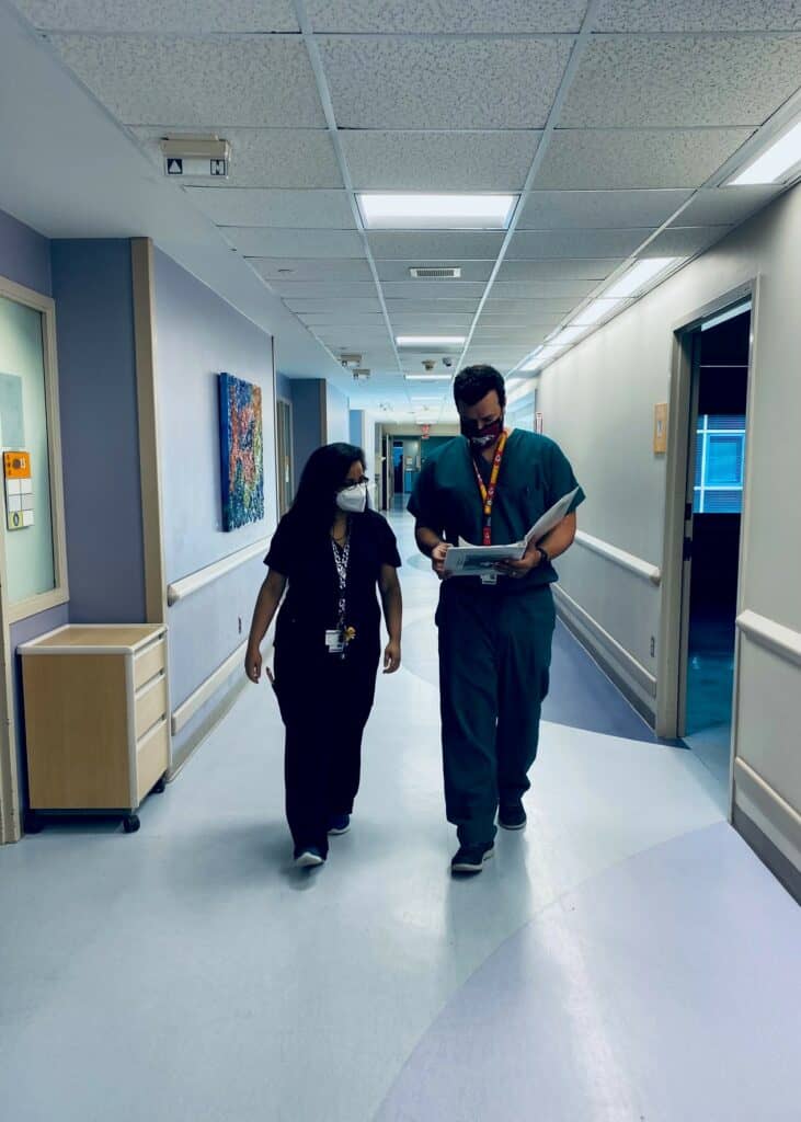 Two Child Neurology Residents walk down a brightly colored hallway reviewing patient information.