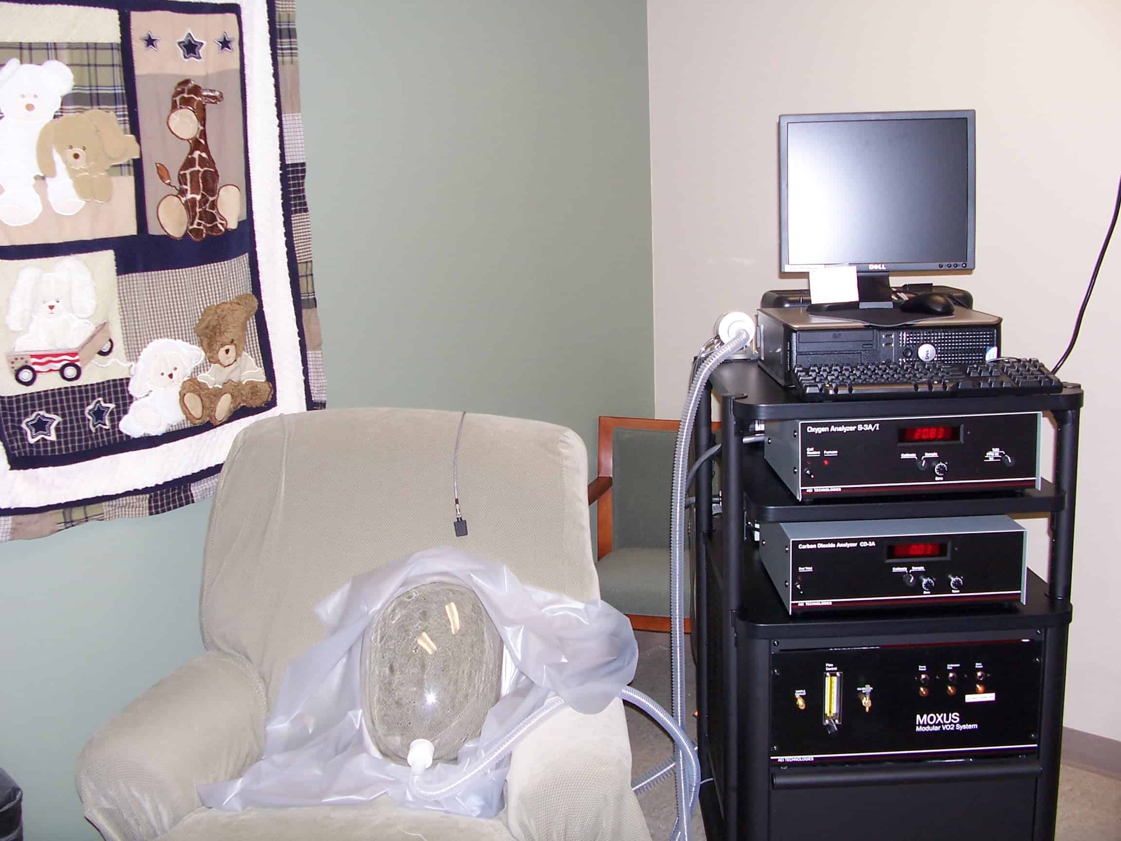 MOXUS hood sitting on a chair next to a computer on a cart it is plugged into