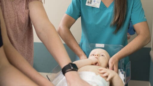child lays supine while body length is measured by three staff members smiling
