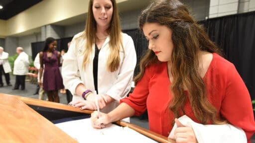 A female graduate signs the book to collect her lab coat before the commencement ceremony