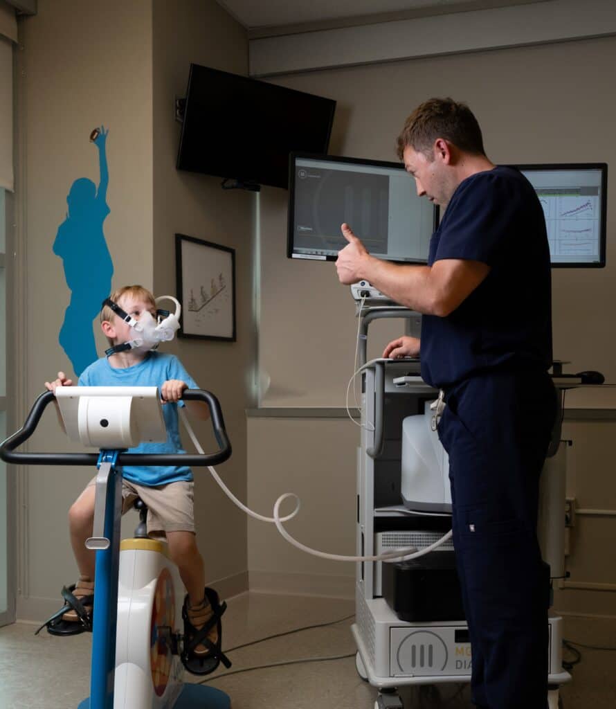 boy on exercise bike with oxygen max looks at a nurse giving thumbs up