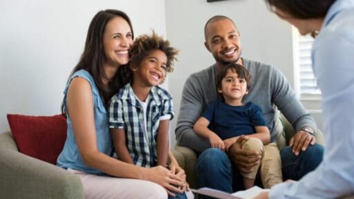 family of four sitting on a couch, smiling at their doctor.