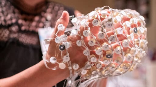 A researcher holds a research device made up of dozens of sensors made to be worn on a patient's head.