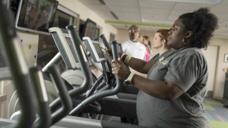 a row of adults on elliptical machines with a trainer