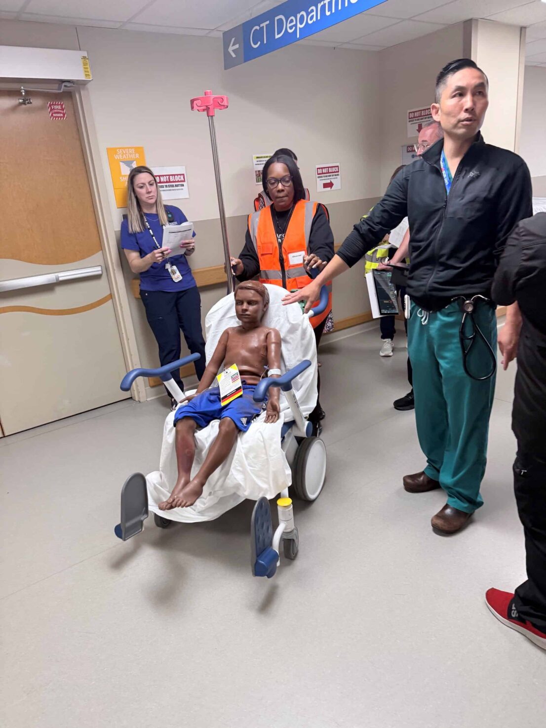 Doctors, nurses and other medical professionals work during an emergency simulation in the Emergency Department. A nurse pushes a pediatric training dummy in a wheelchair.