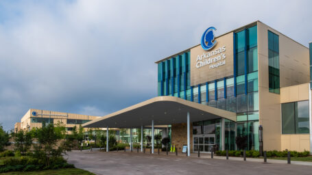 The remodeled exterior of Arkansas Children's Hospital. A large valet area with a covered entrance leads to the new, brighter and more inviting patient entrance. The new outpatient center, Champions Pavilion, rises in the background of the shot.