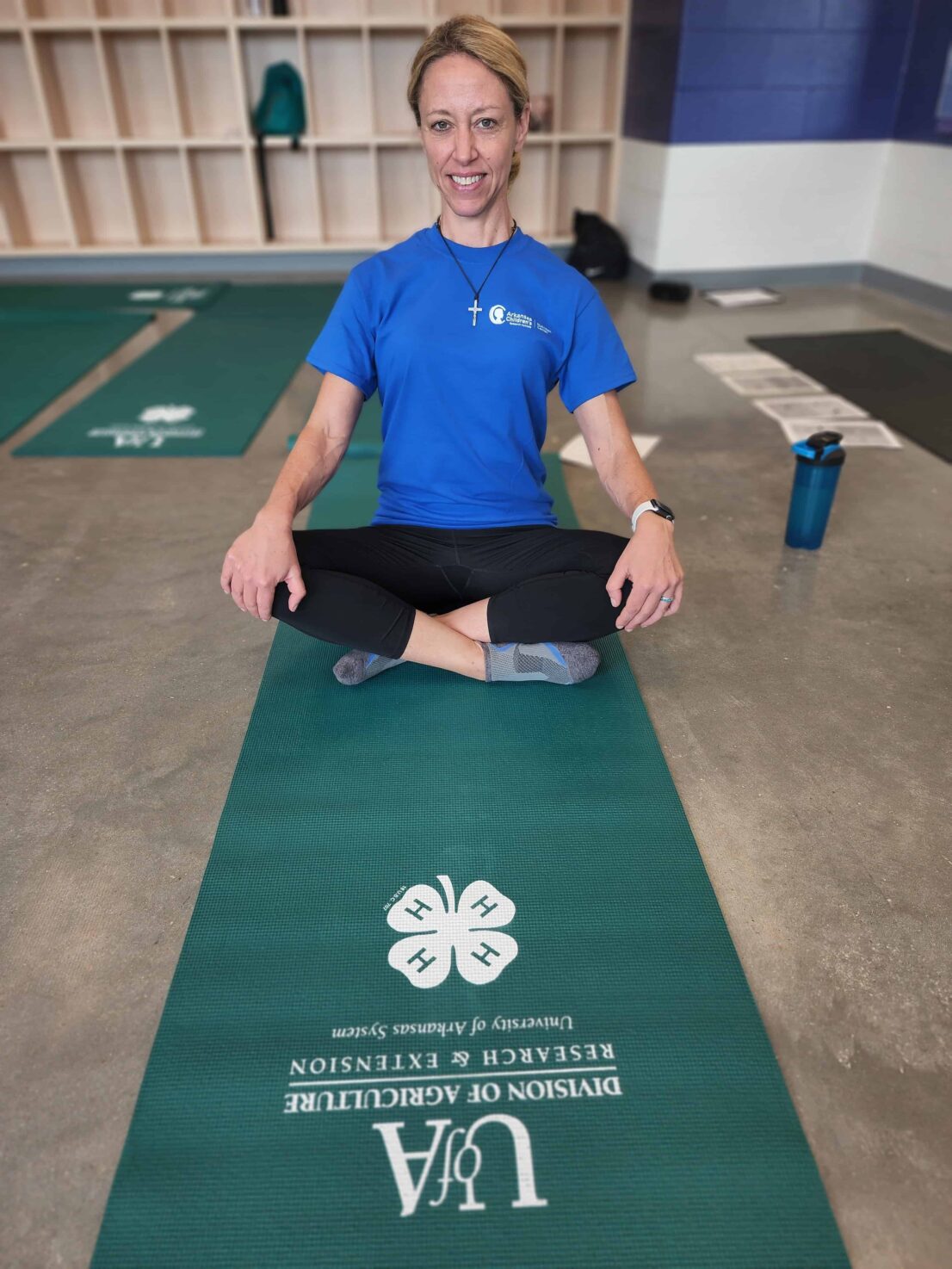 an ACNC employee sits upright on a green yoga mat, she has blonde hair and is smiling