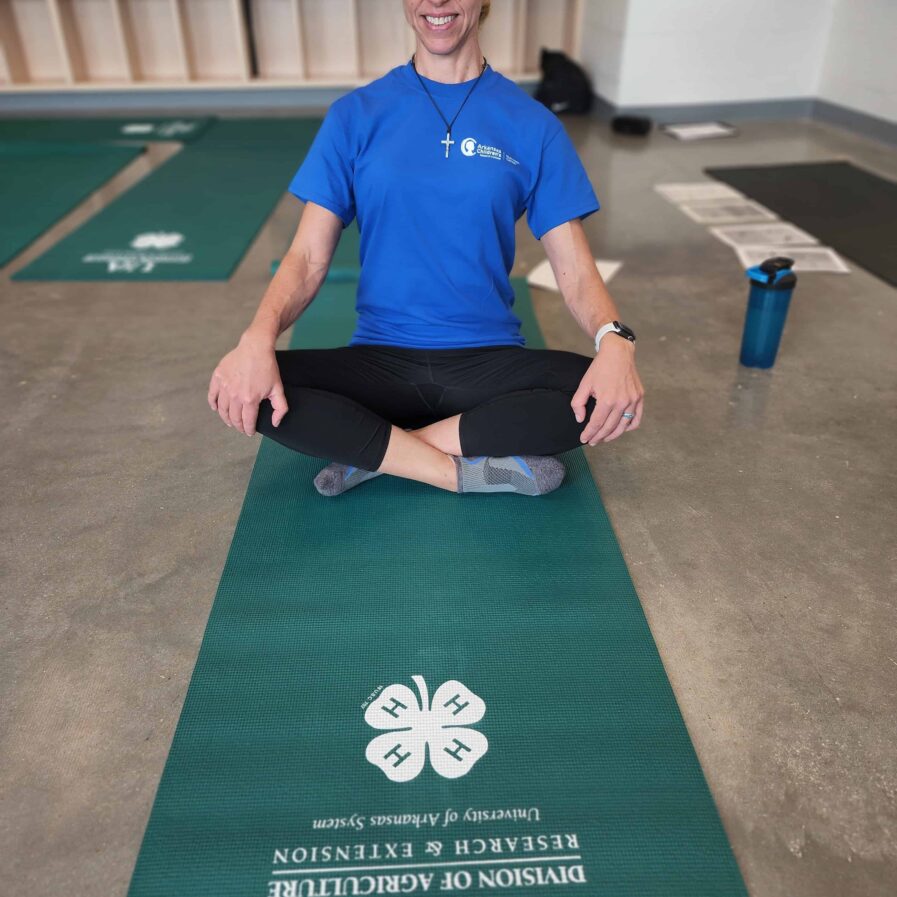 an ACNC employee sits upright on a green yoga mat, she has blonde hair and is smiling