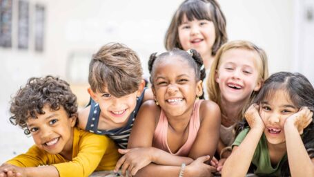 A small group of six daycare friends lay huddled in closely stacked on top of one another as they pose for a portrait