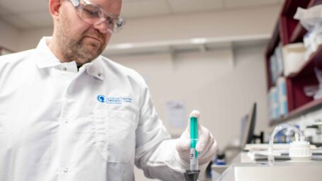 Dr. Craig Porter in a white coat handles a sample in the lab