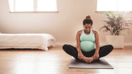 pregnant woman in green sits on a yoga mat in a beige room