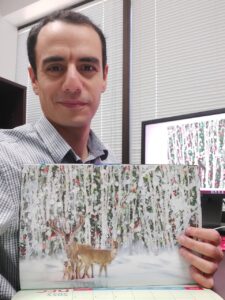 Dr. Fouda holding a printed picture of deer with a holiday background