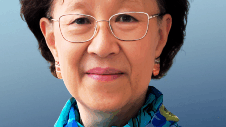 headshot of Dr. Ho. in front of a blue background with a dark blue blazer and scarf on