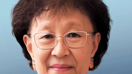 headshot of Dr. Ho. in front of a blue background with a dark blue blazer and scarf on