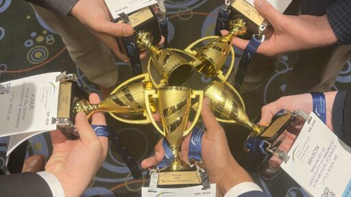 Close up of students' hands holding trophies and their conference name tags. The photo is taken from above, and the students are holding the trophies together.