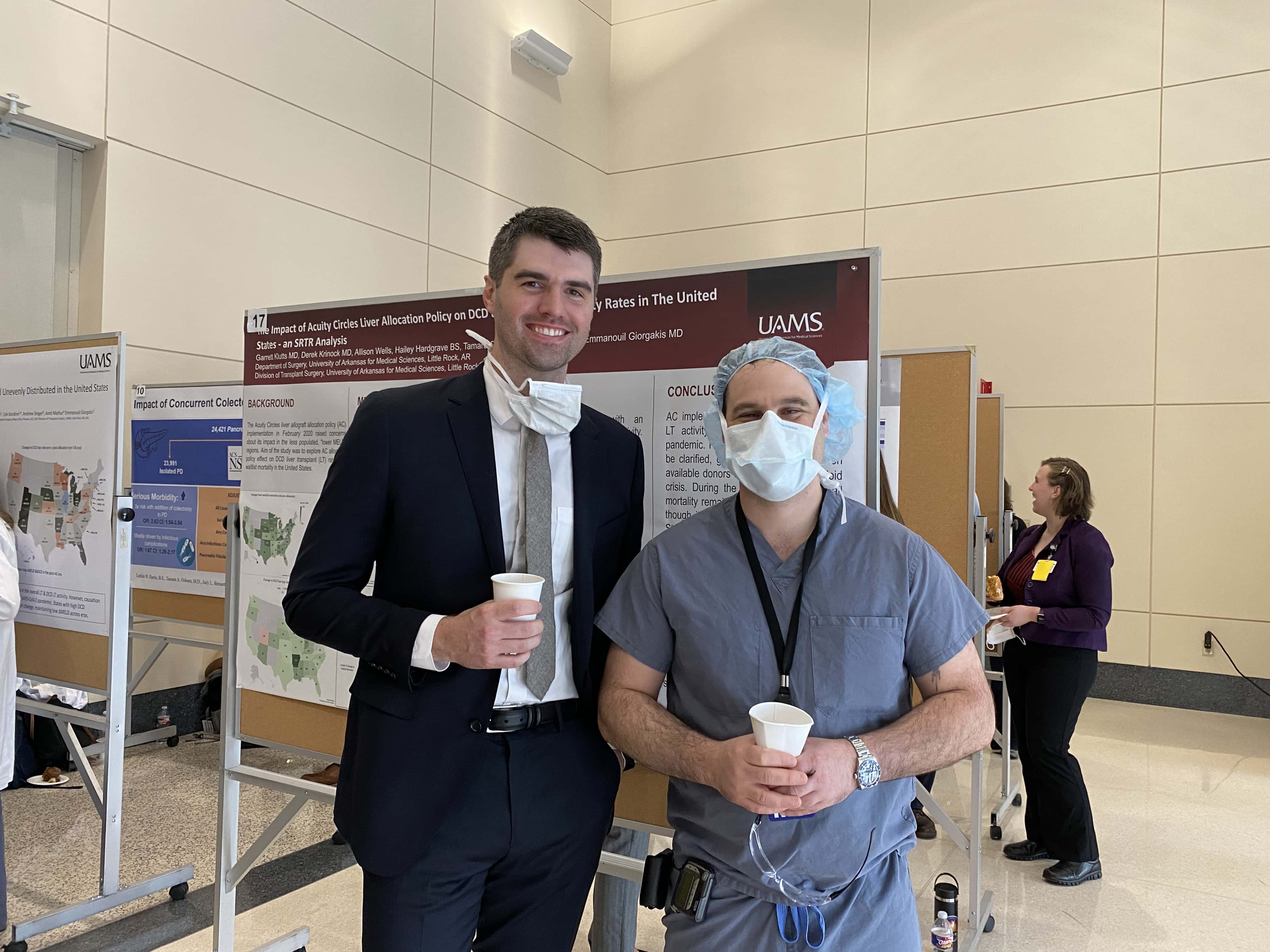 Two people, one in a suit, and one in scrubs, in front of a research poster