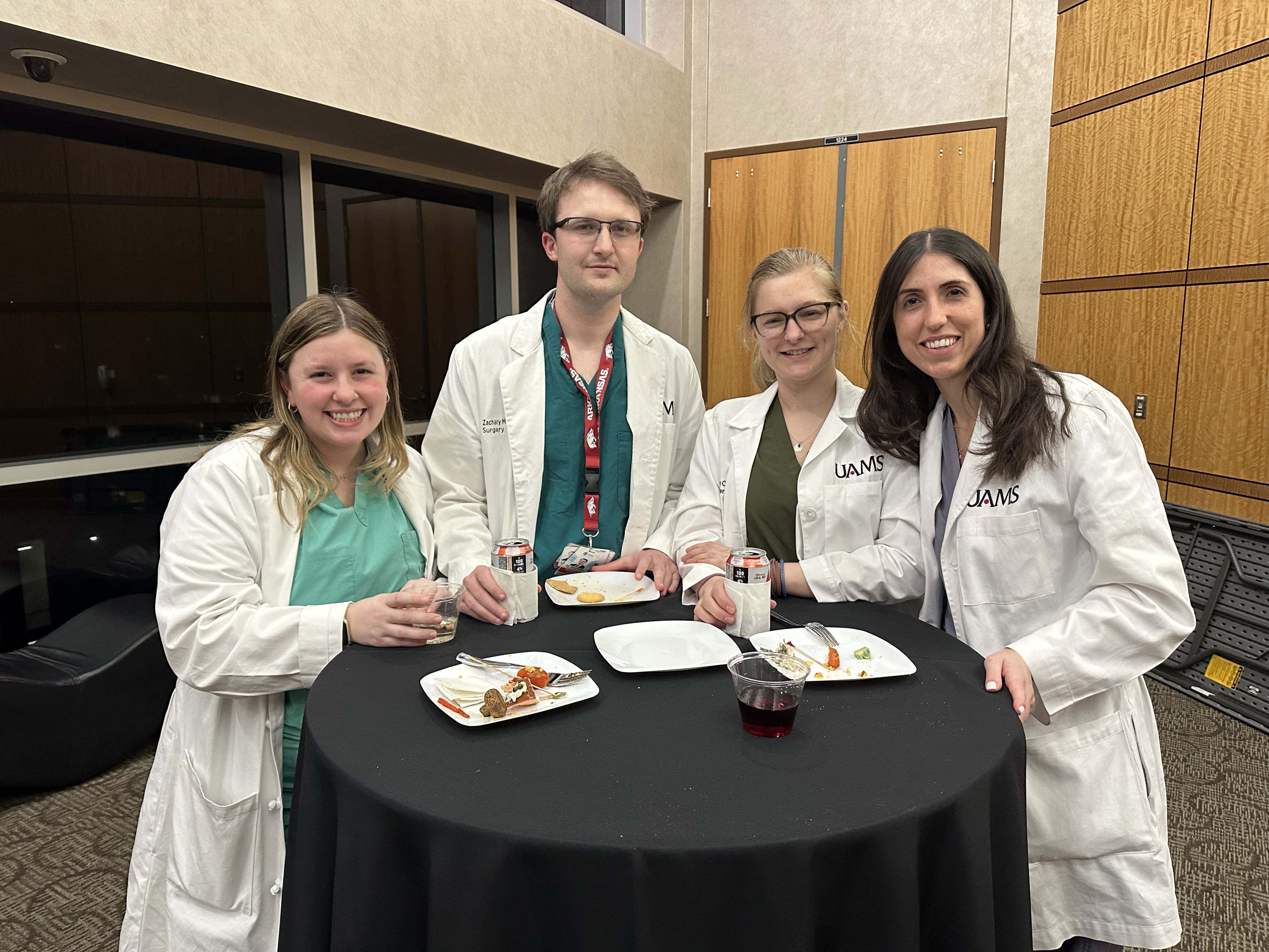 Group of faculty and students posing around a small table at a reception