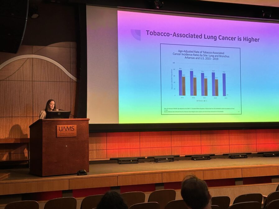 Dr. Marino speaks at a podium in an auditorium. There is a large screen showing her slide