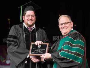 Student holding award, shaking hands with faculty member