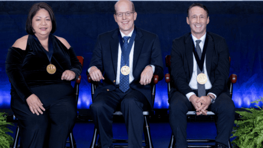 Drs. Maya Lopez, Ron Sanders Jr. and David Spiro wearing endowment medallions and seated in ceremonial chairs on a stage.