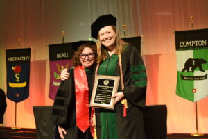 Faculty member poses with a graduating student, the student is holding the Susan Smyth, M.D./Ph.D. Award plaque