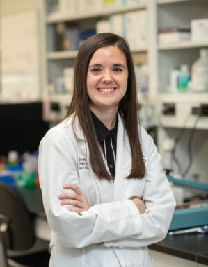 Sydnye Shuttleworth, wearing a white coat, poses in the Brian Koss lab