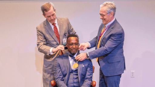 Dr. Cam Patterson and Dr. Steven Webber place medallion on Dr. Corey Montgomery as he sits in ceremonial chair at his investiture.