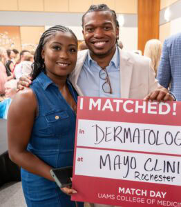 Happy student and family member or significant other holding up a sign that says "I Matched" Dermatology at the Mayo Clinic in Rochester.