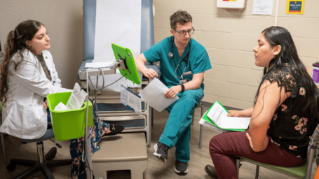 Medical student in scrubs and Pharmacy student wearing white coat visit with patient in clinic