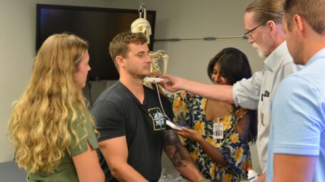 Dr. Kevin Phelan uses a handheld ultrasound on a student in 2025. The students are part of the accelerated 3-year program in primary care. They are entering freshmen who started class a couple of weeks earlier than their peers in the 4-year track. Photo is at Northwest Arkansas Campus.